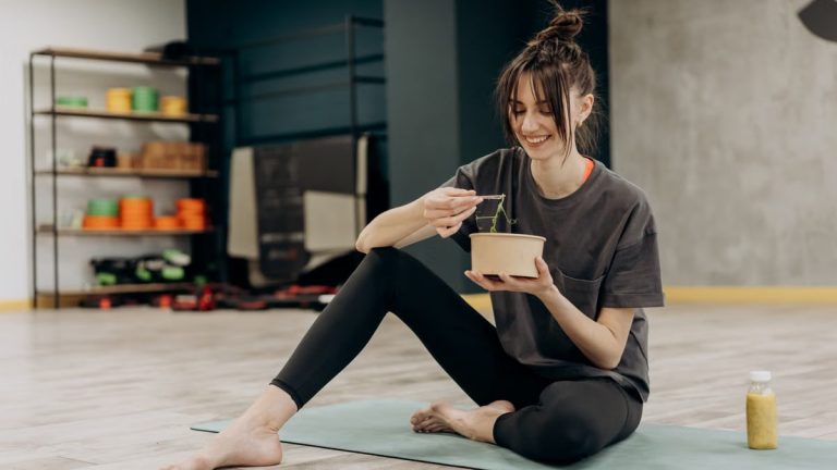 Young woman enjoying a healthy salad after exercising indoors. Promotes a balanced diet and fitness lifestyle.